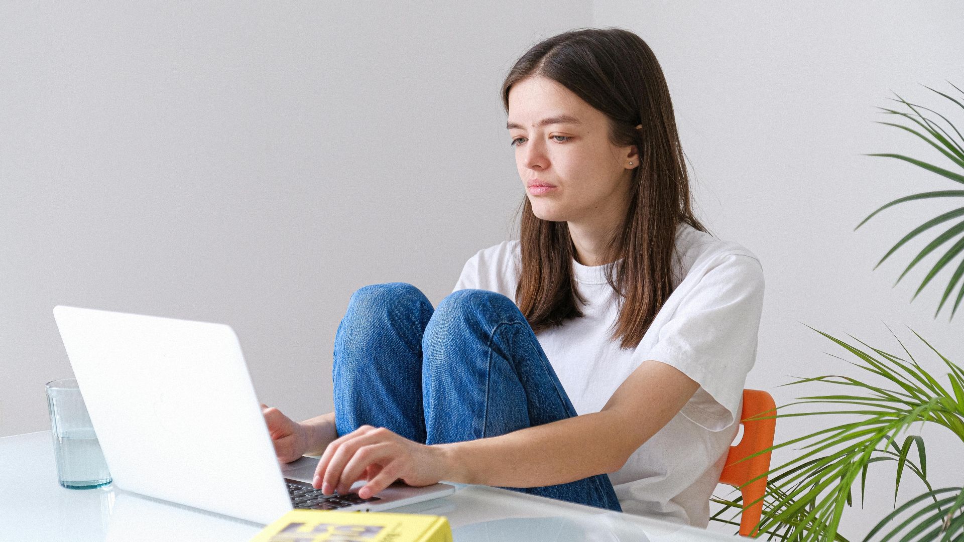 Young woman in blue jeans working on laptop from home office, embracing remote work lifestyle.