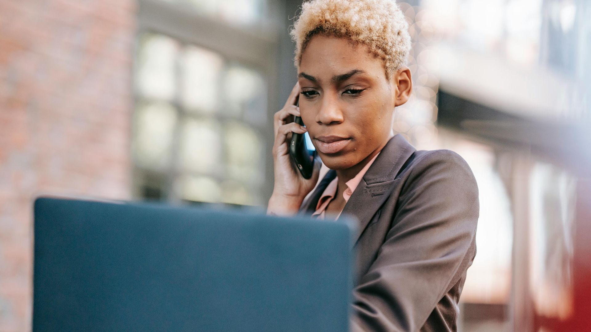 Focused professional woman multitasking using a laptop and phone outdoors.
