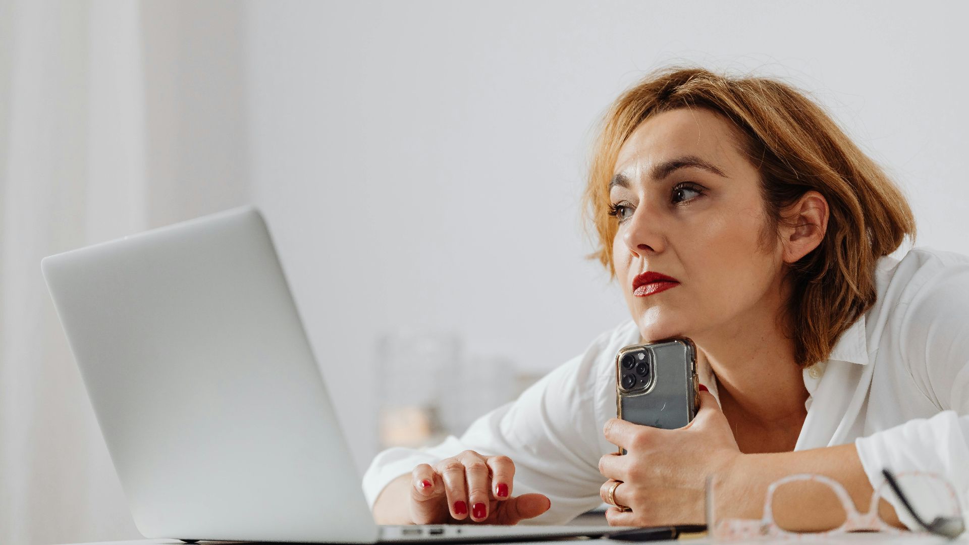 Businesswoman using laptop and mobile phone at modern office desk.