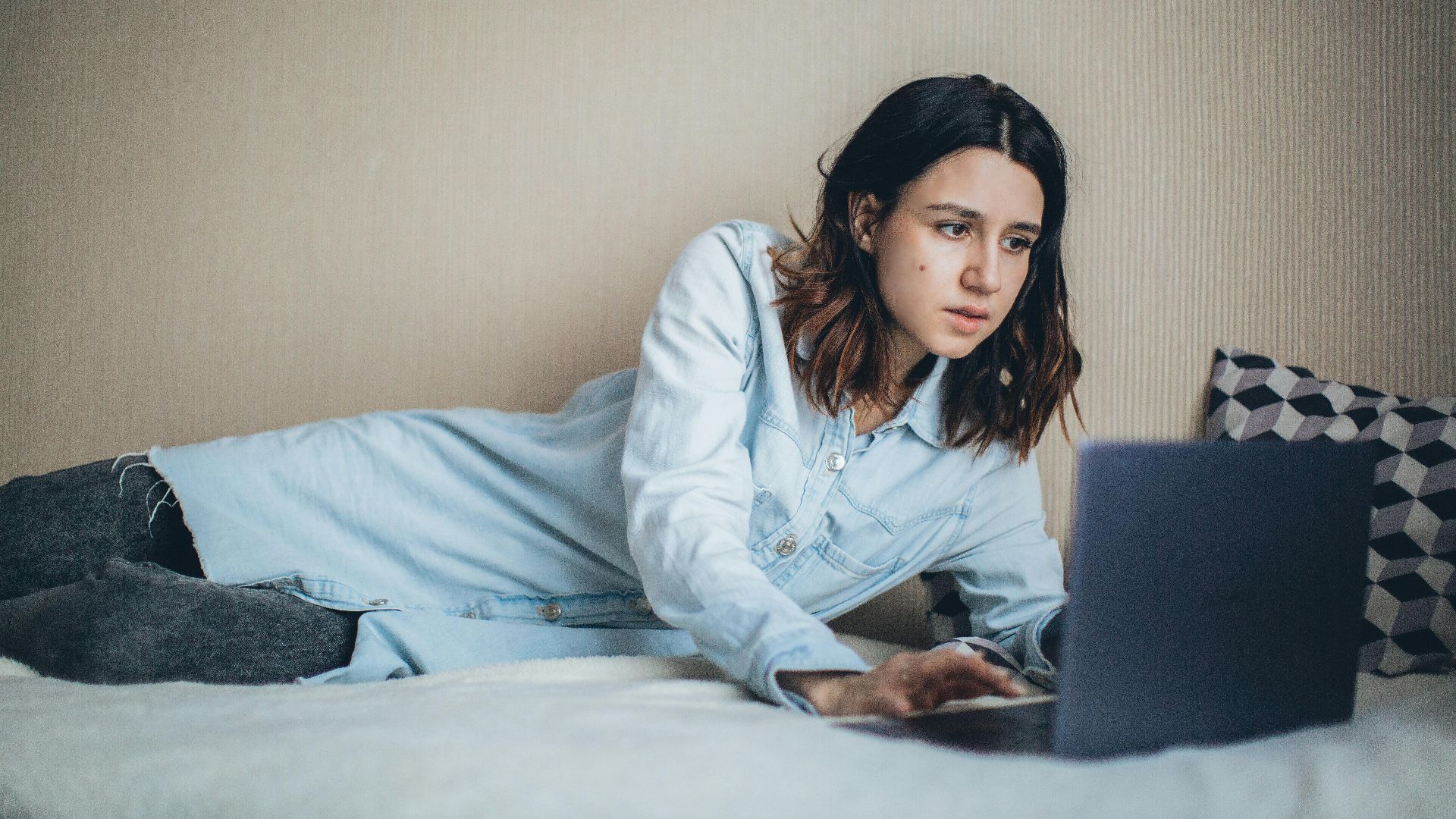A woman relaxes in bed while working on a laptop, embodying freelance lifestyle and remote work convenience.