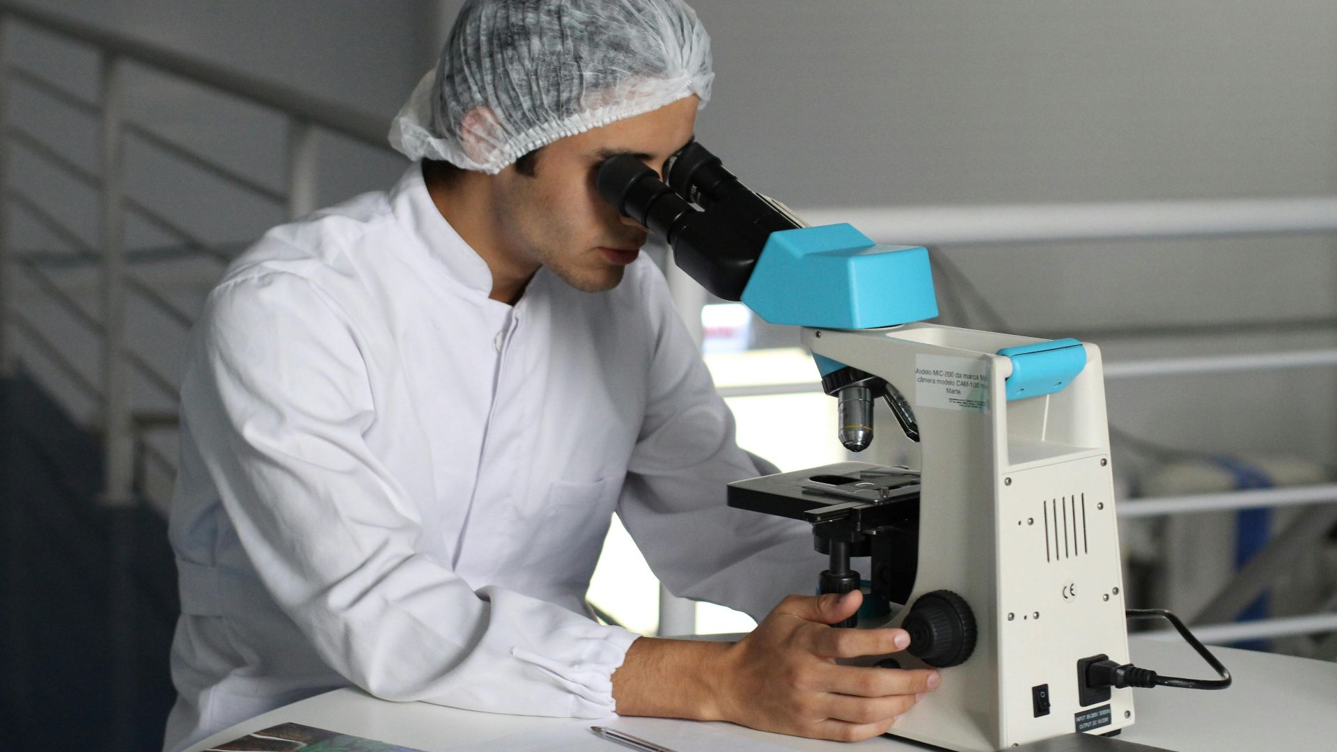 Scientist in a lab coat using a microscope to conduct research, focusing on healthcare improvements.