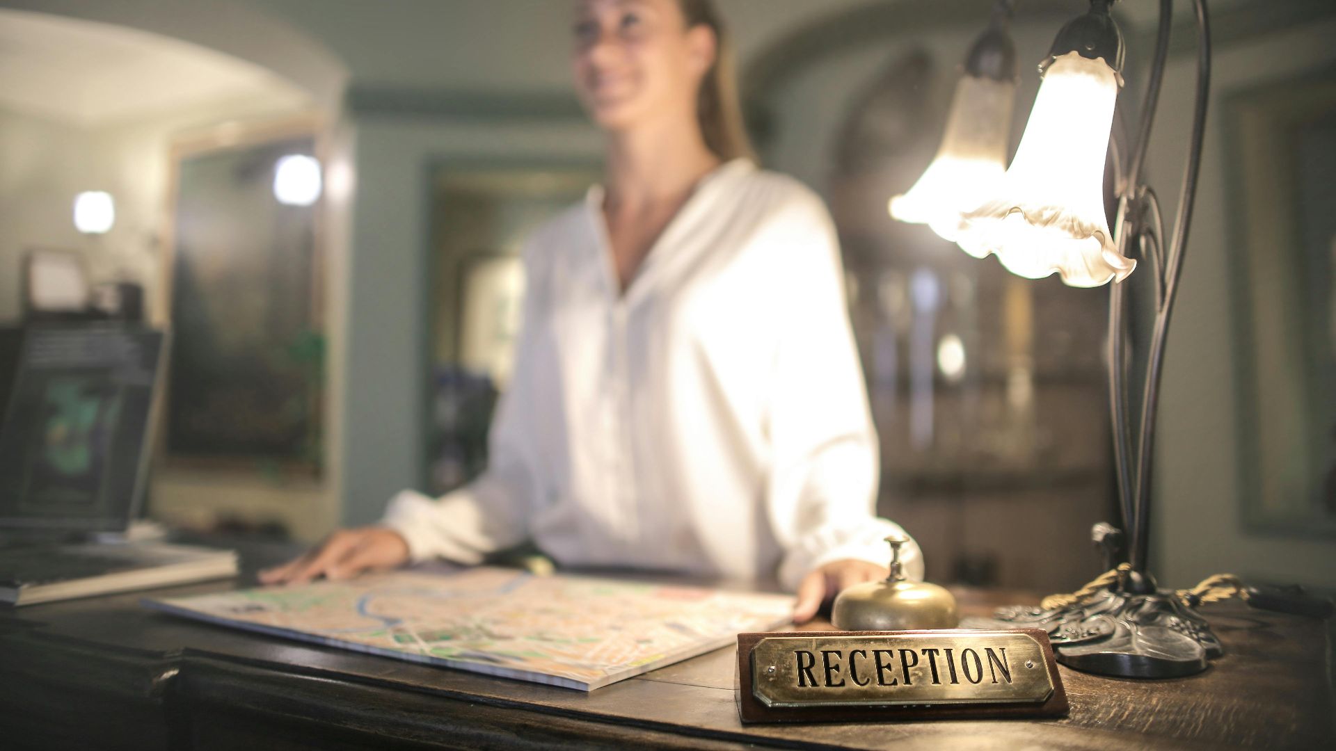 A concierge stands at a hotel reception desk under ambient lighting, ready to assist guests.
