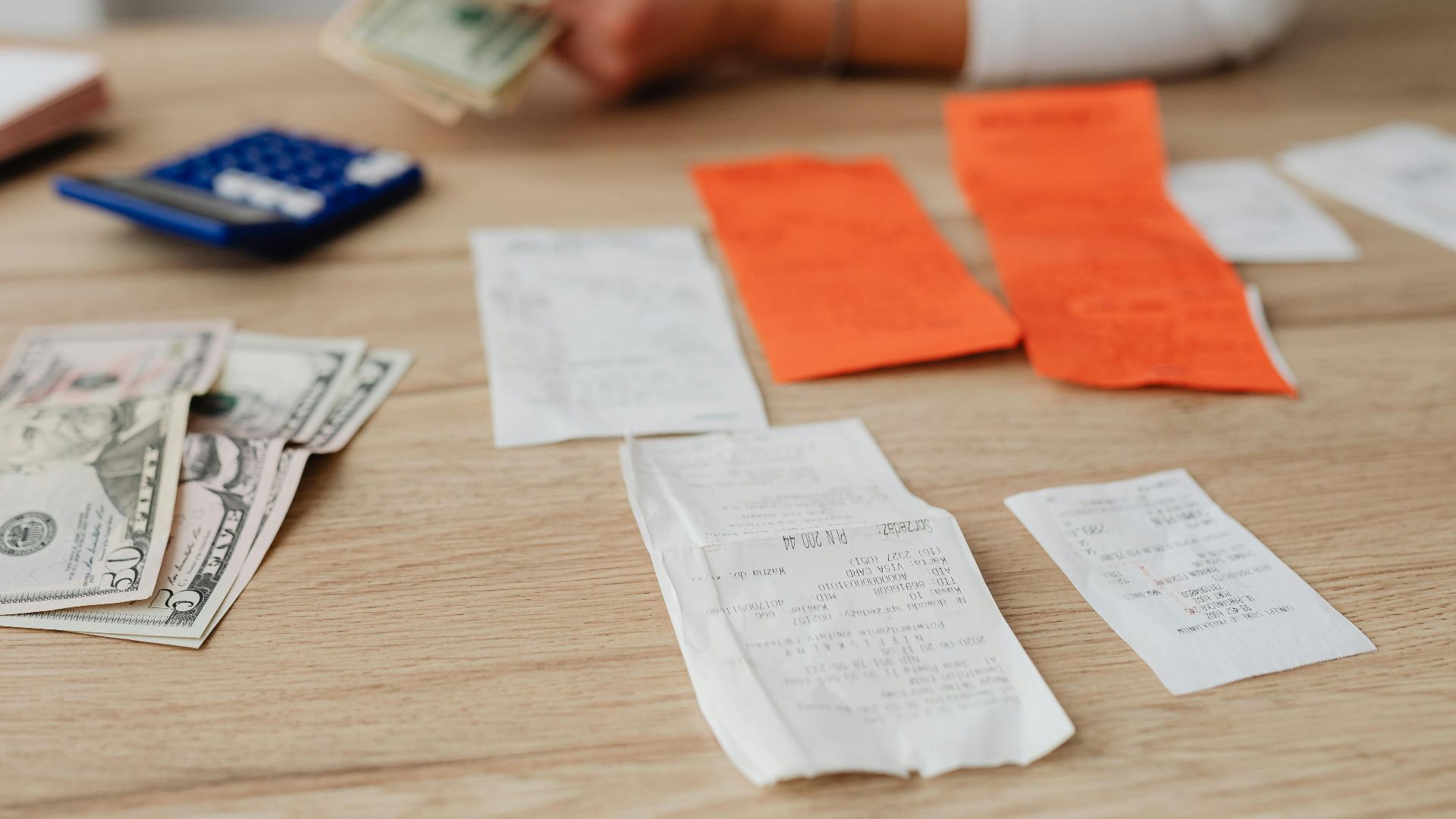 A person using a calculator and cash to plan a household budget.