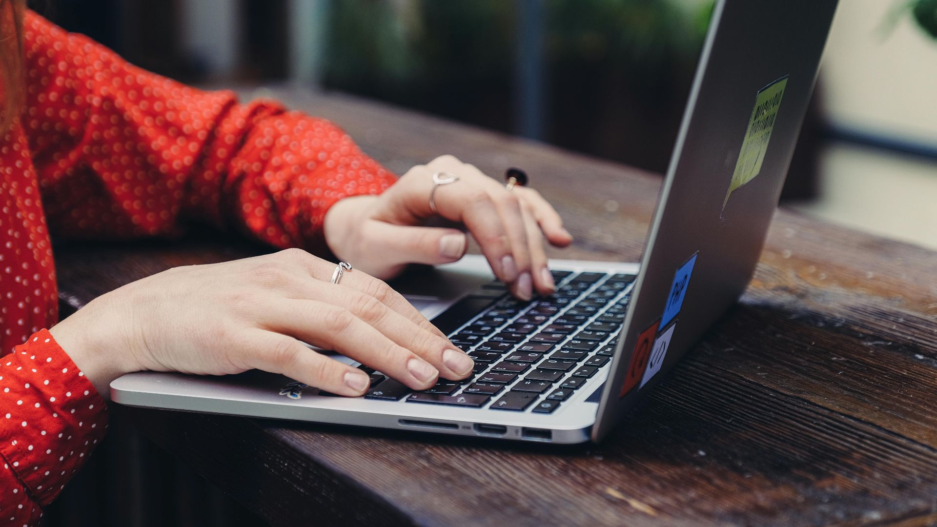 Close-up of hands typing on a laptop placed on a wooden table outdoors.