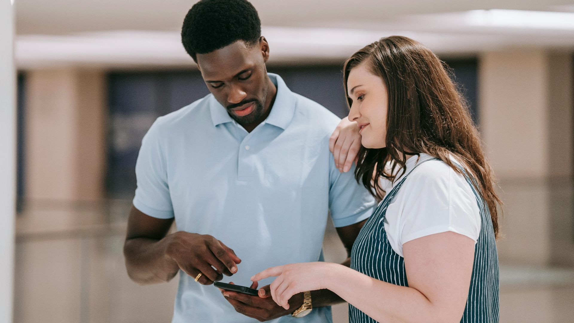 A couple indoors discussing something on a smartphone with focused expressions.