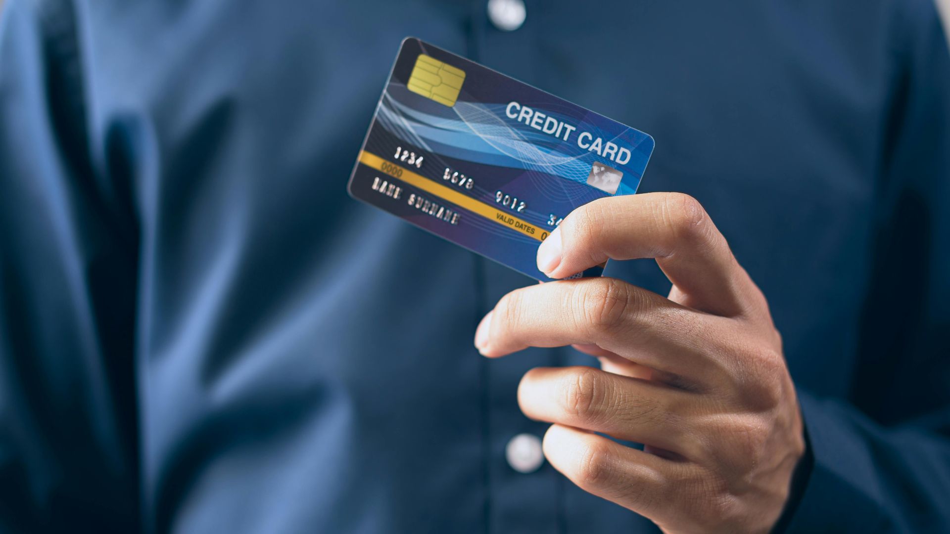 Close-up of a person holding a credit card in a hand, wearing a button-up shirt.