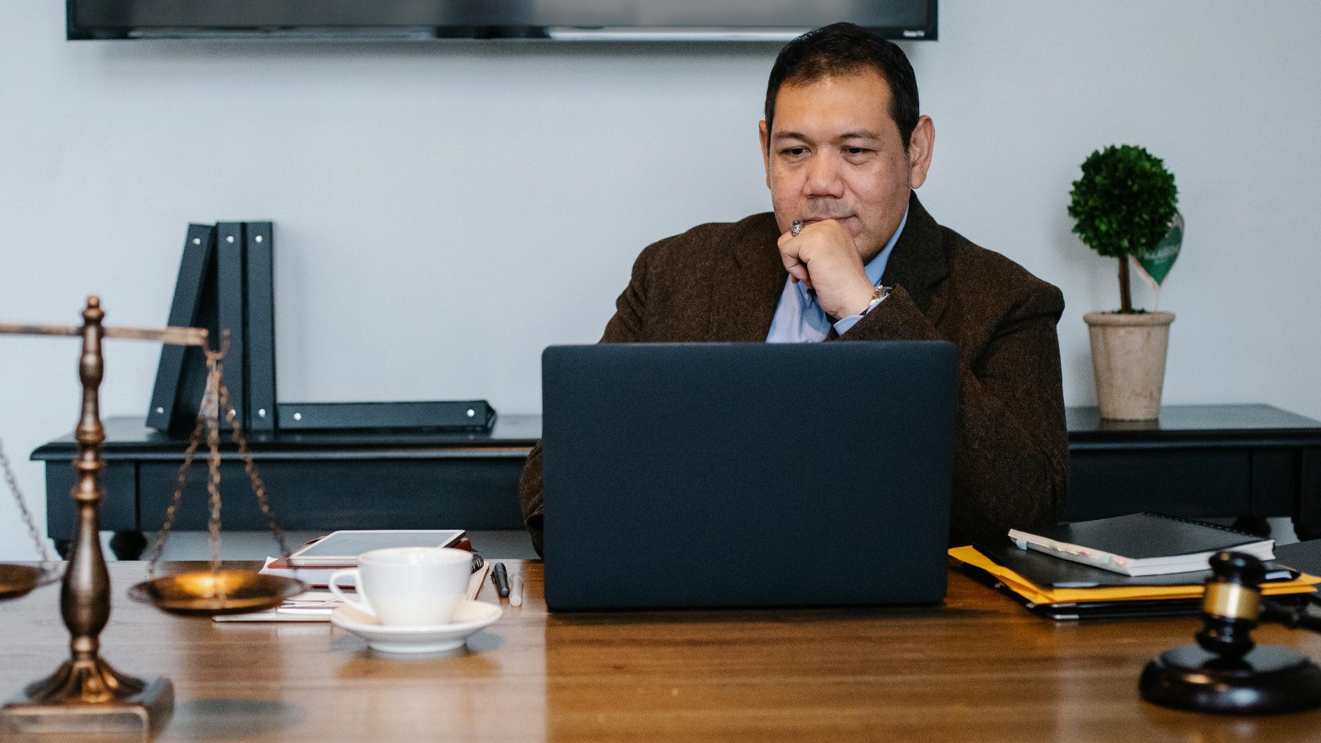 Serious ethnic mature man in formal outfit working with netbook at table with gavel