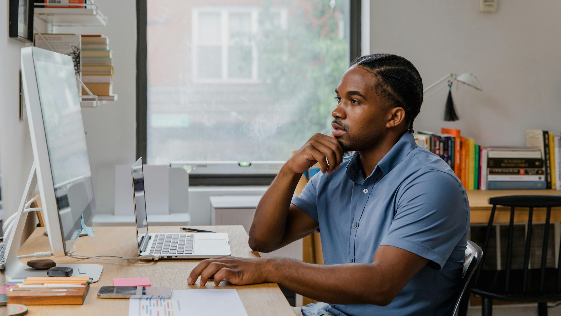 Adult man concentrating at his home office desk with computer, books, and natural light.