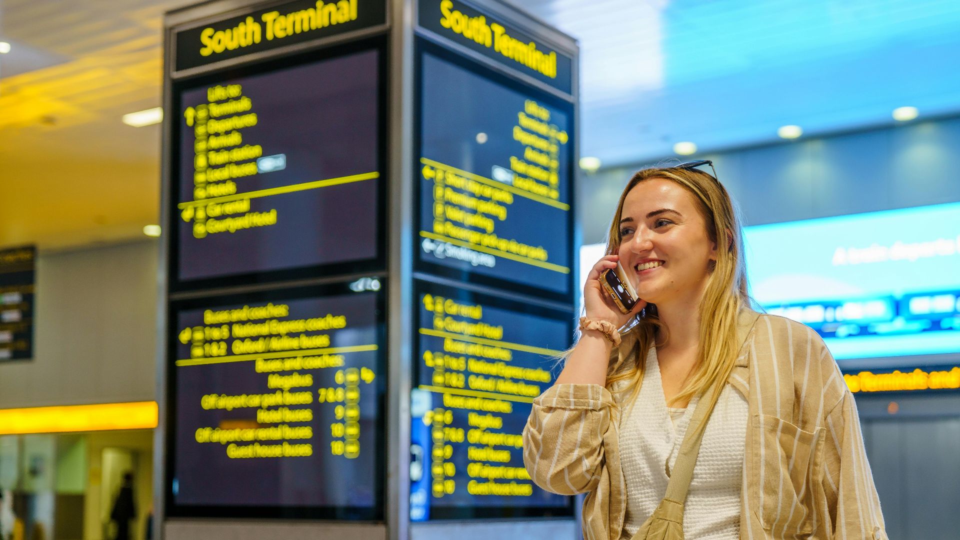 Smiling woman on phone in South Terminal of Gatwick Airport, Horley, enjoying her travel experience.