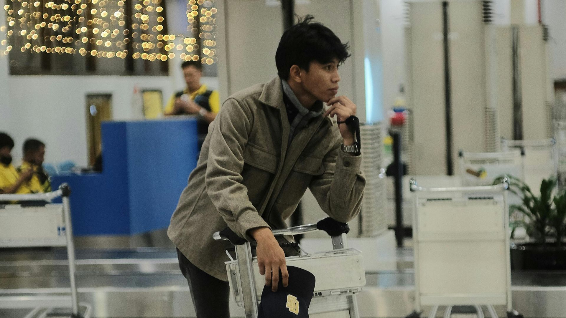 Man in casual attire standing by luggage cart in airport terminal.