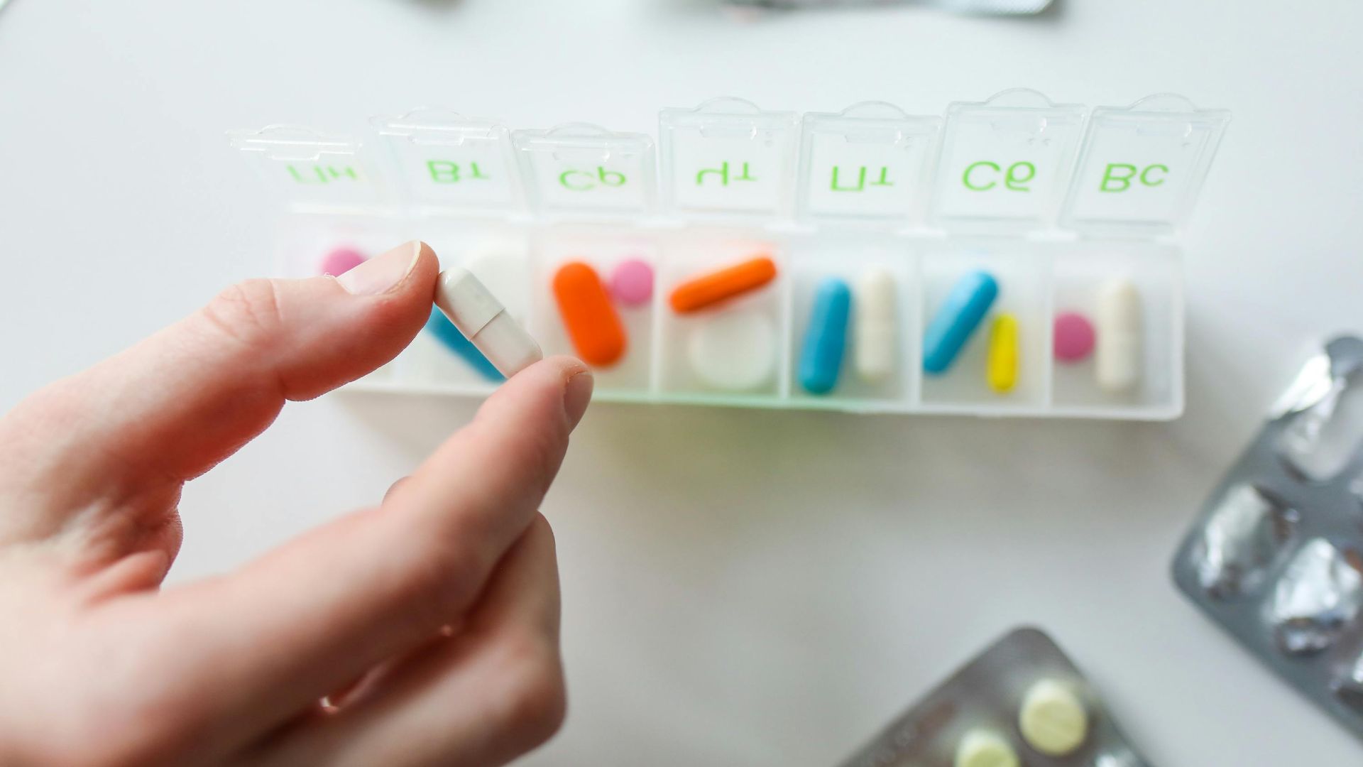 Close-up of a hand selecting a pill from a weekly pill organizer, illustrating daily health and medication routines.