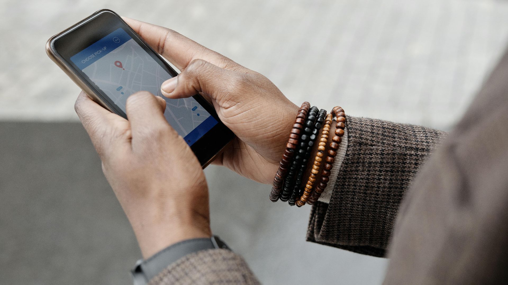 Close-up of hands with bracelets navigating on smartphone using GPS app outdoors.
