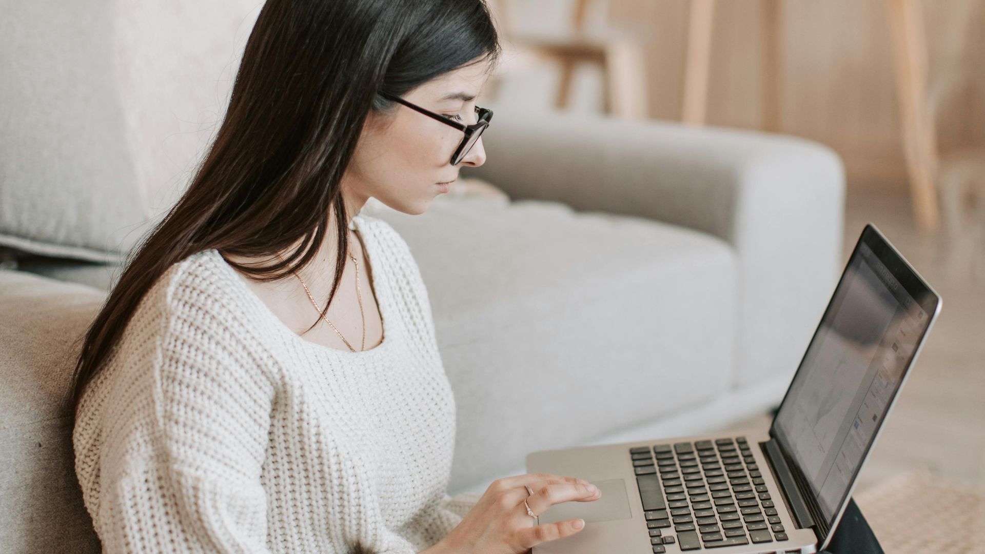 A young woman sits on the floor using a laptop, working remotely in a cozy living room.