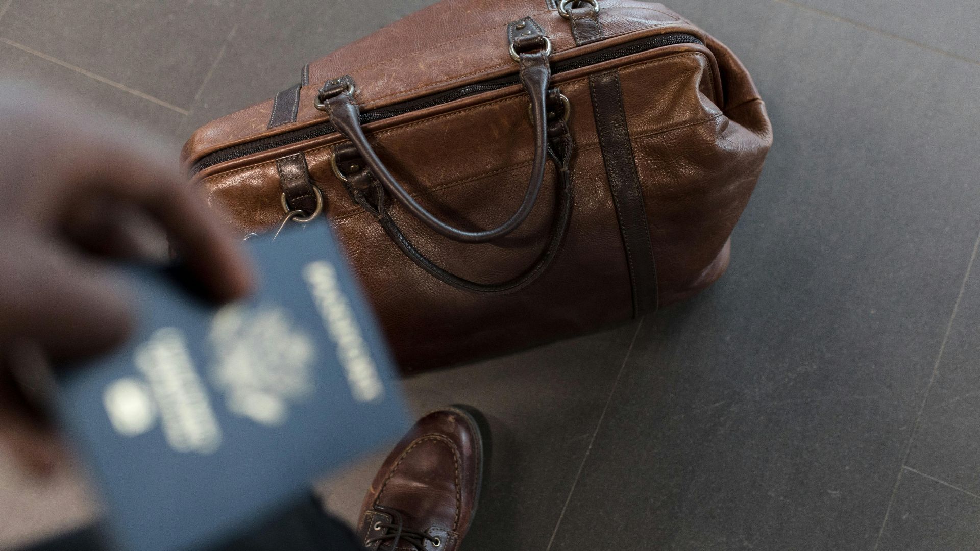 Brown leather bag with passport in an airport setting, ideal for travel and fashion themes.