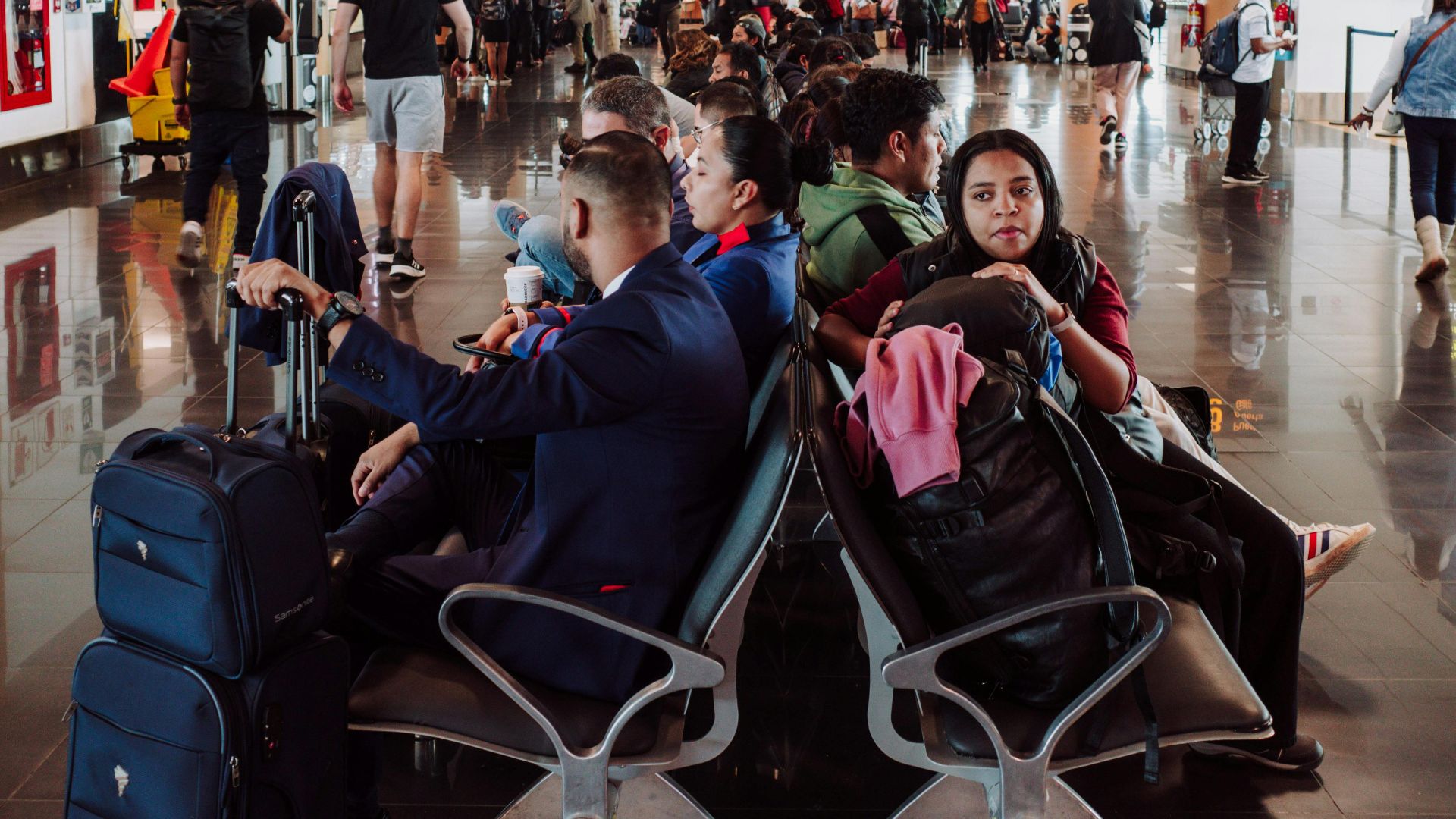 Passengers waiting in a busy airport terminal seating area, with luggage in the modern airport.