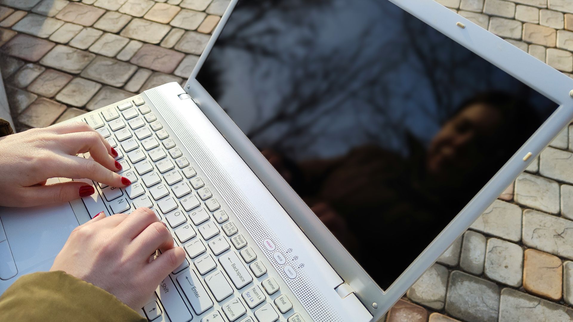 a woman is typing on a laptop outside