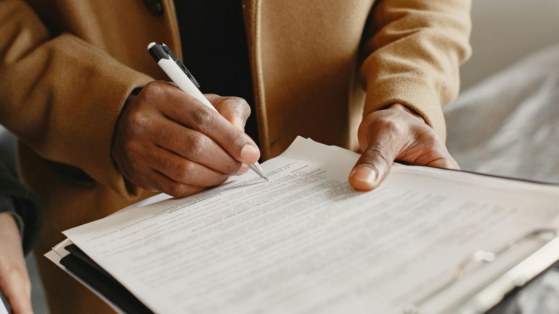 Close-up of a person signing a contract on a clipboard, focusing on legal formalities.