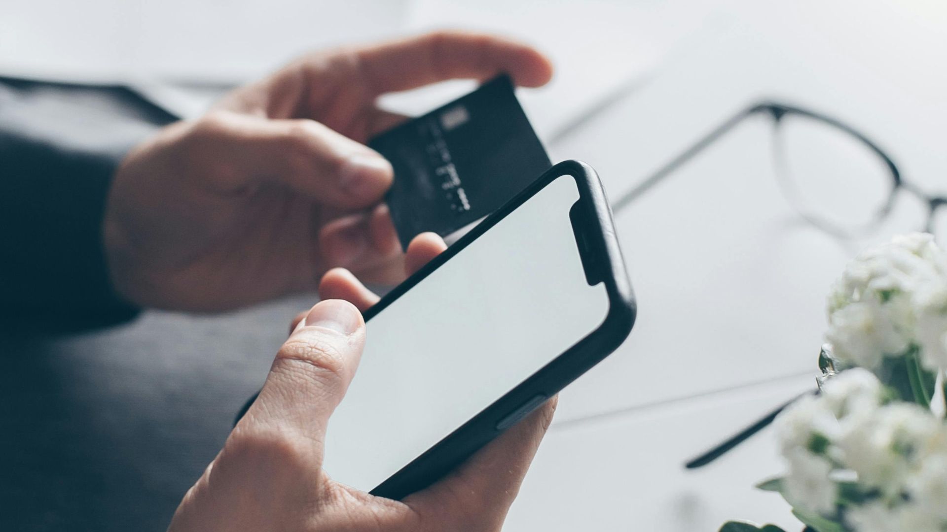 Close-up of hands holding a smartphone and a credit card, implying online payment.