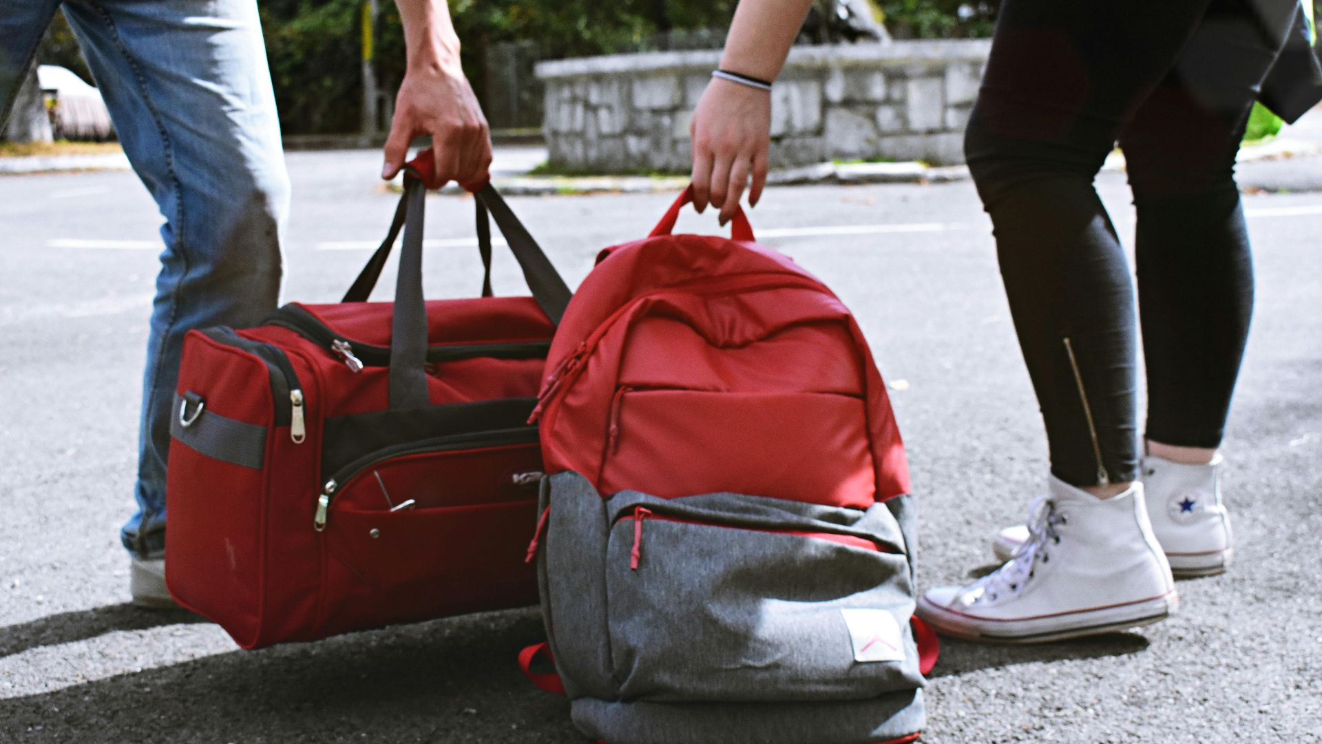 Two travelers holding red bags on a street, symbolizing travel and exploration.