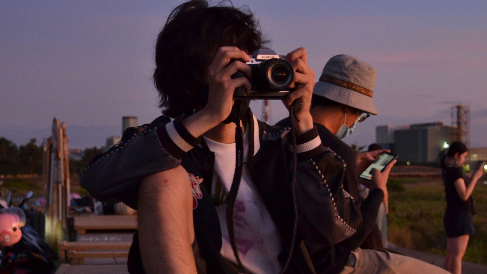 A young adult captures photos during sunset outdoors, creating a serene and artistic scene.