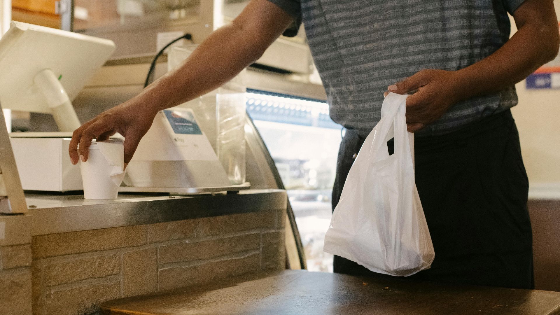 Unrecognizable male picking up takeaway order and cup in a casual cafe setting.