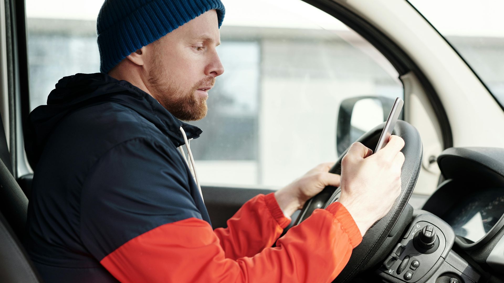 Distracted driver uses a smartphone in a car, highlighting road safety concerns.