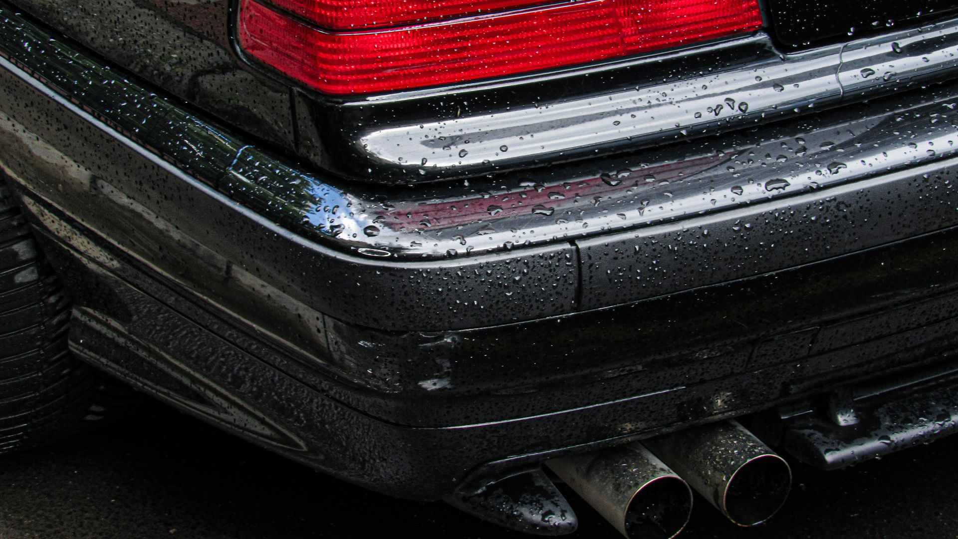 Detailed shot of a wet car bumper showing red and amber tail lights post-rain.