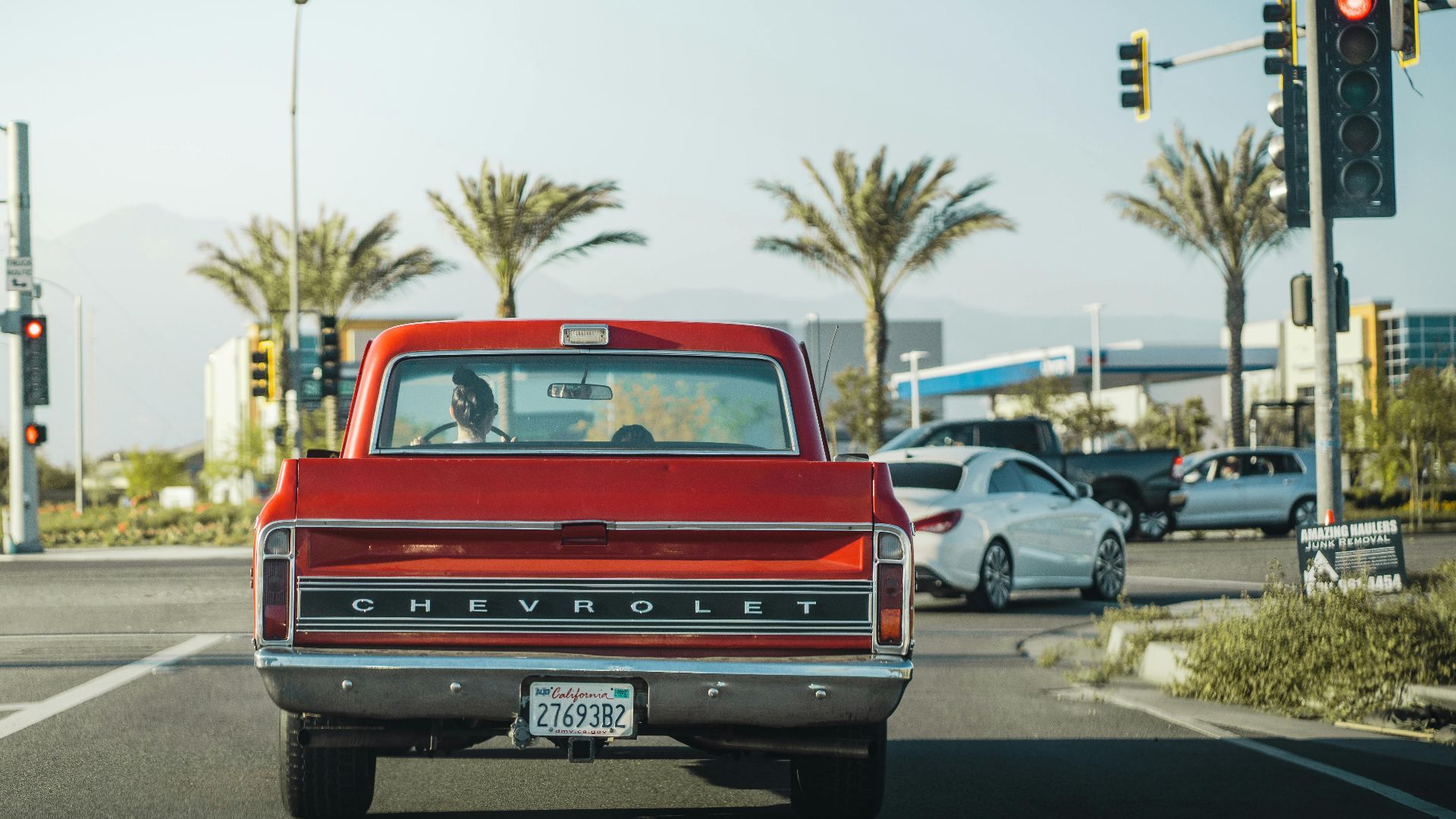 Red vintage Chevrolet truck at traffic light in Los Angeles street backdrop with palm trees.