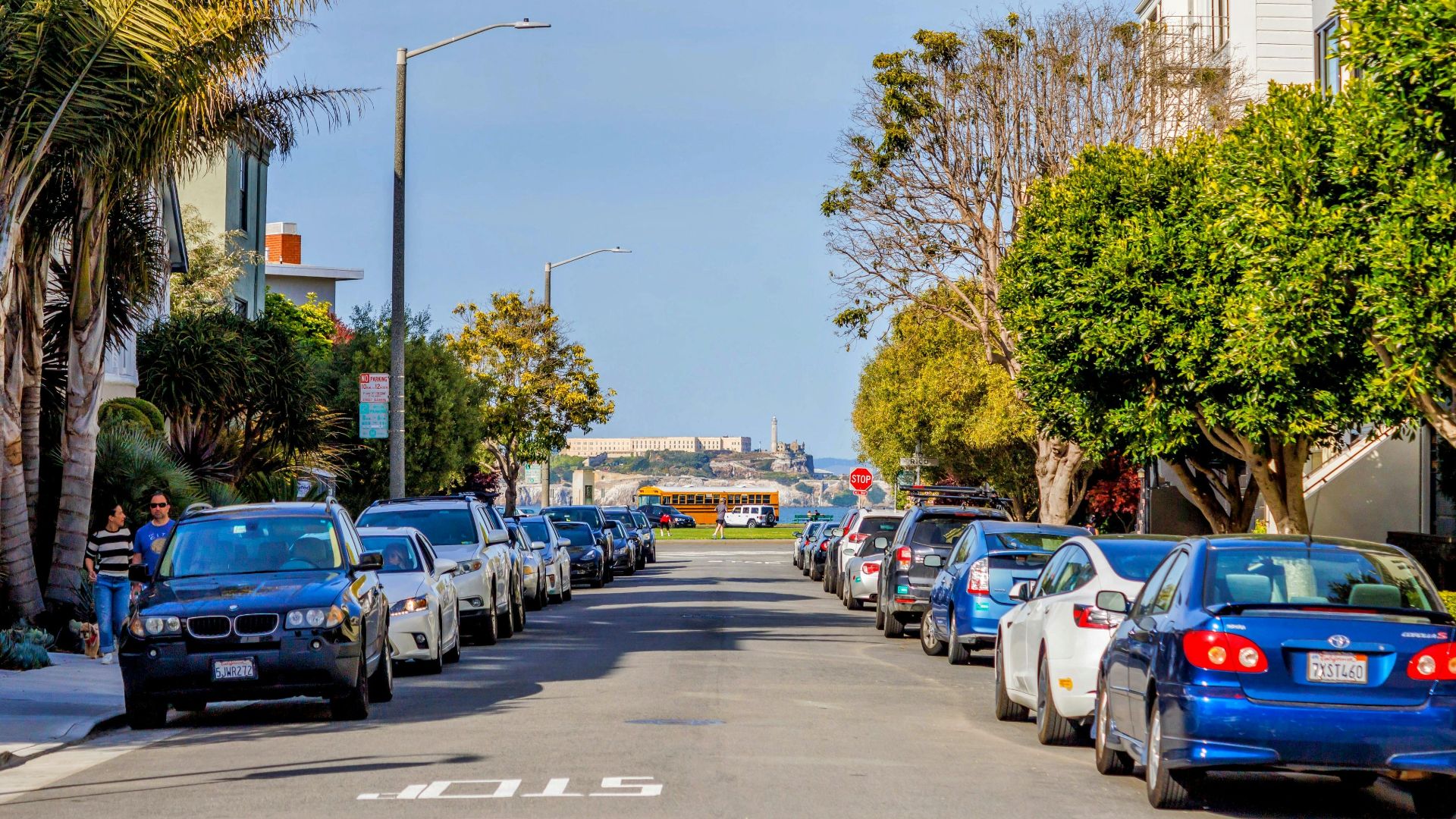 Street view with parked cars and Alcatraz Island in the distance.