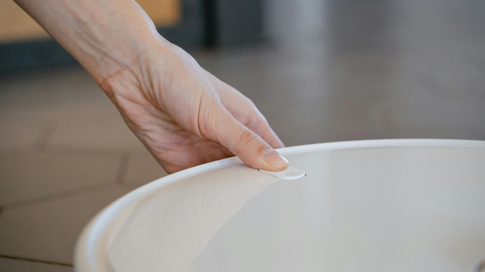 A close-up of a hand gently holding the white lid of a kitchen pot.