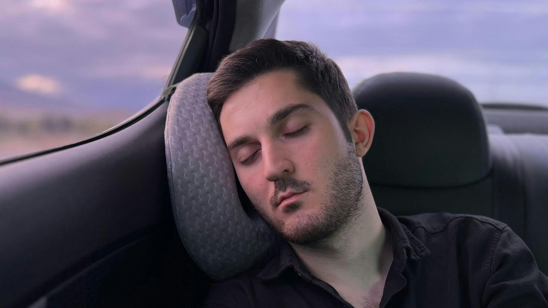 Young man in black shirt sleeping in backseat of a car during twilight in Sijazan, Azerbaijan.