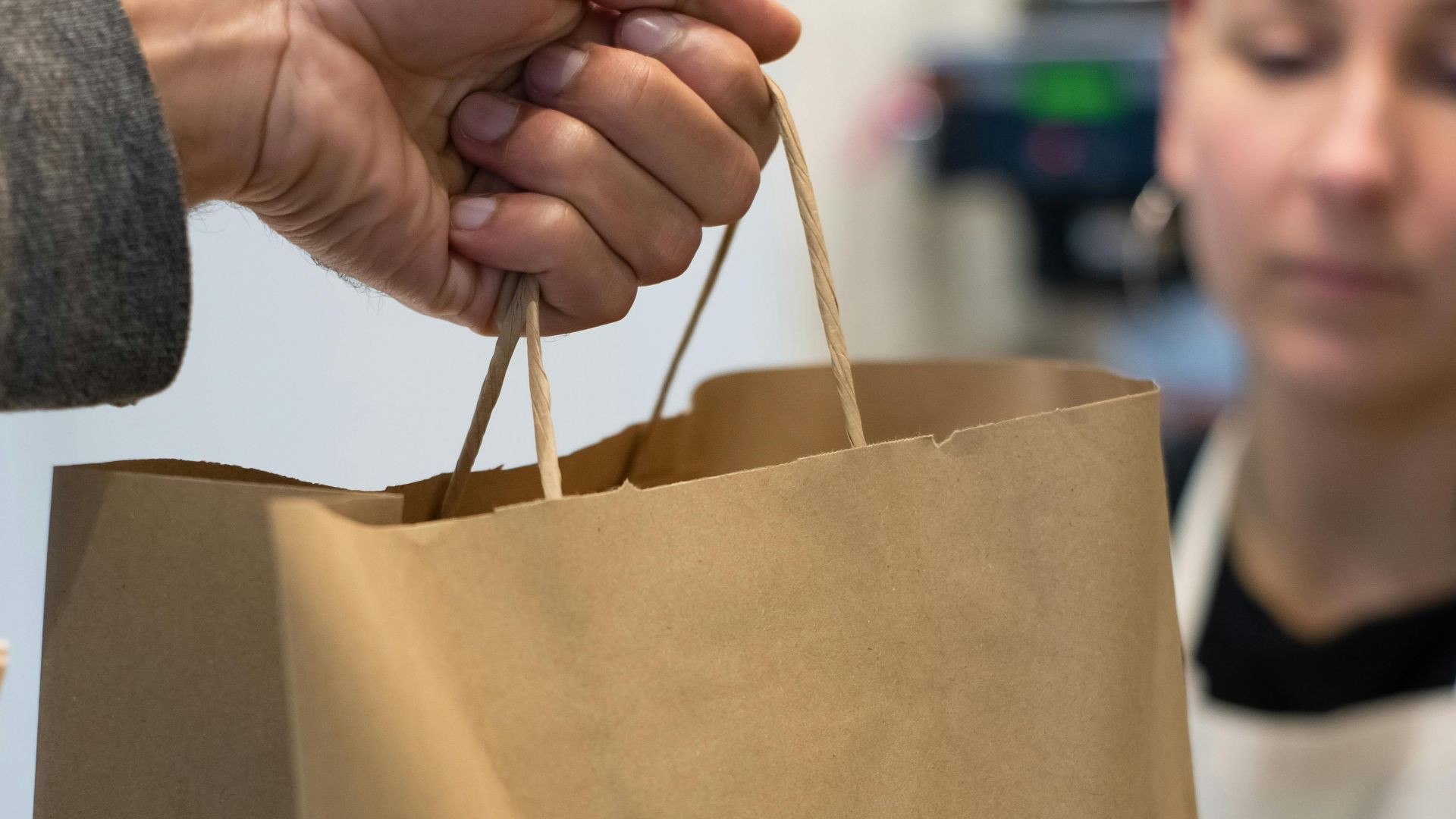 Close-up of a handover of a paper bag in a café, depicting takeaway service.