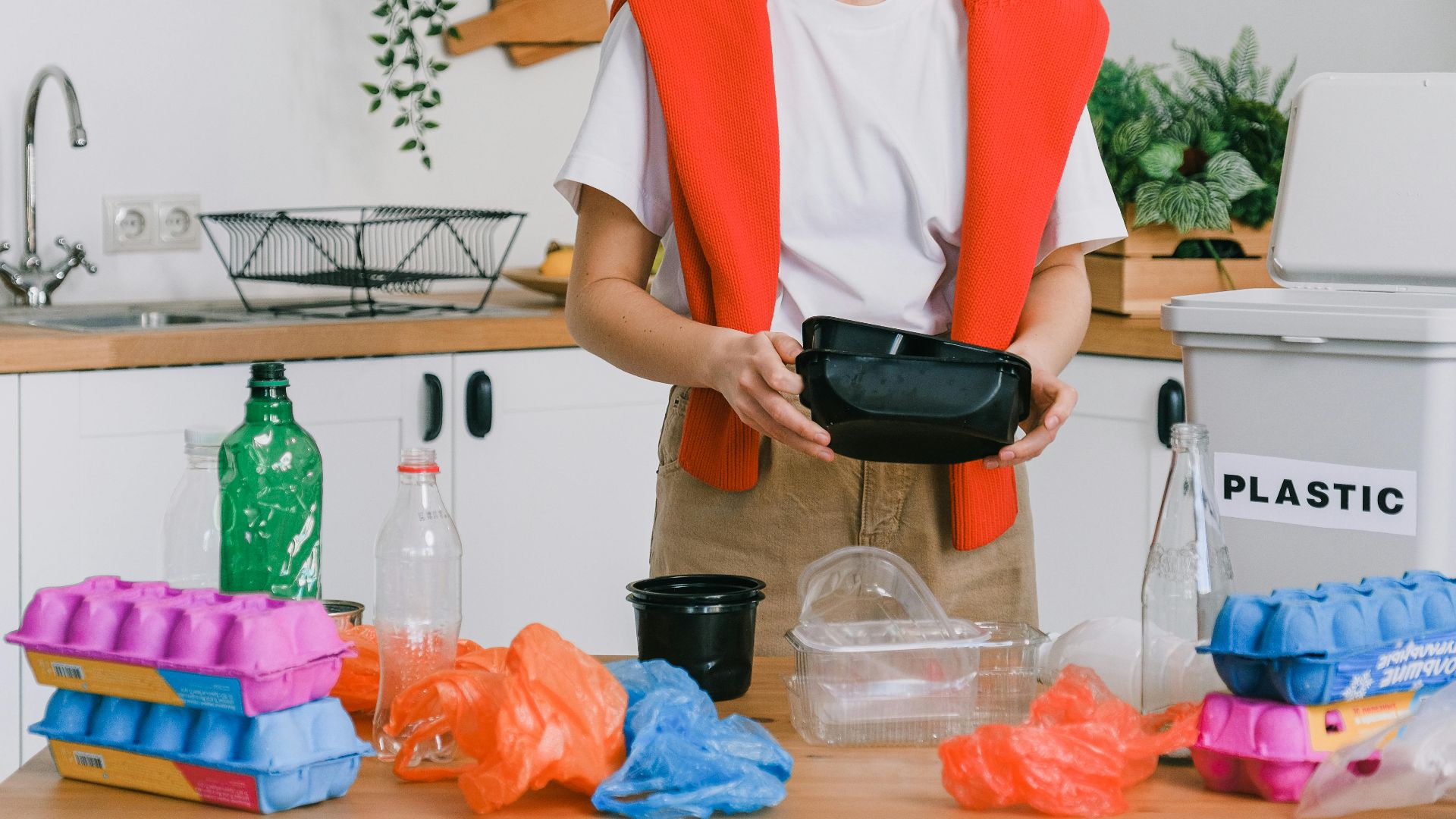 Eco friendly young female in casual clothes standing and sorting recyclable trash in light kitchen in daytime