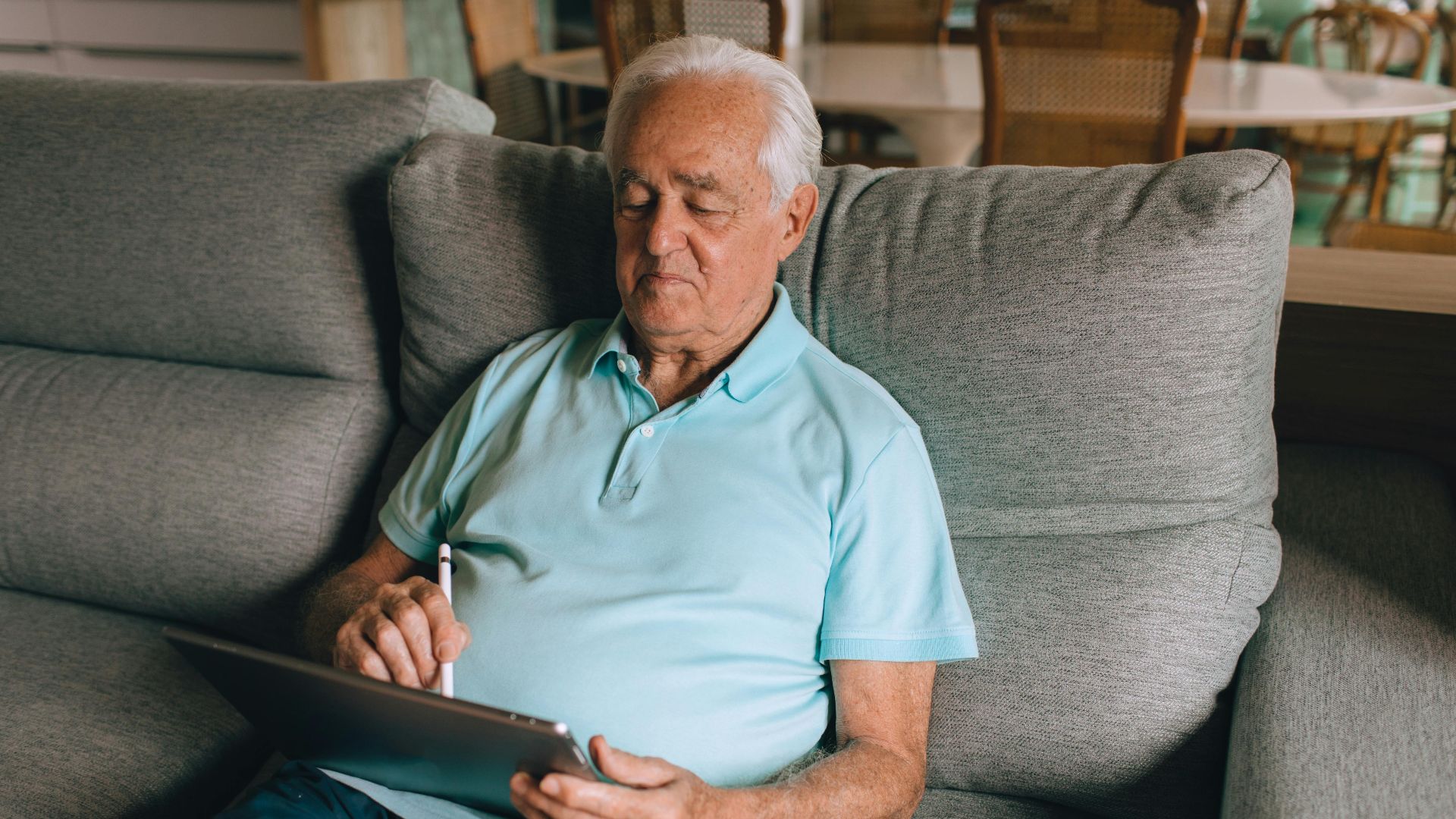 Elderly man using a tablet on a sofa, enjoying leisure time at home.