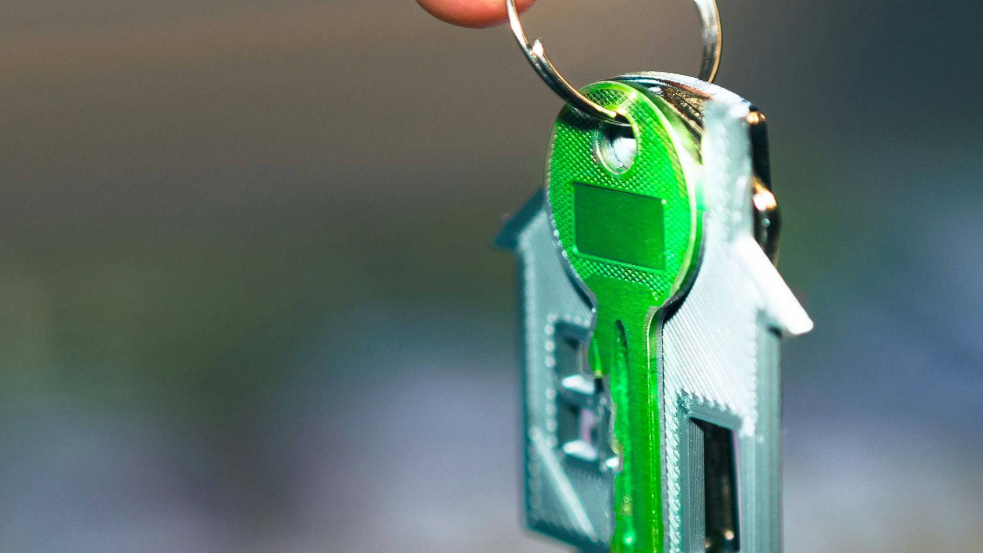 A hand holding a green key to a house