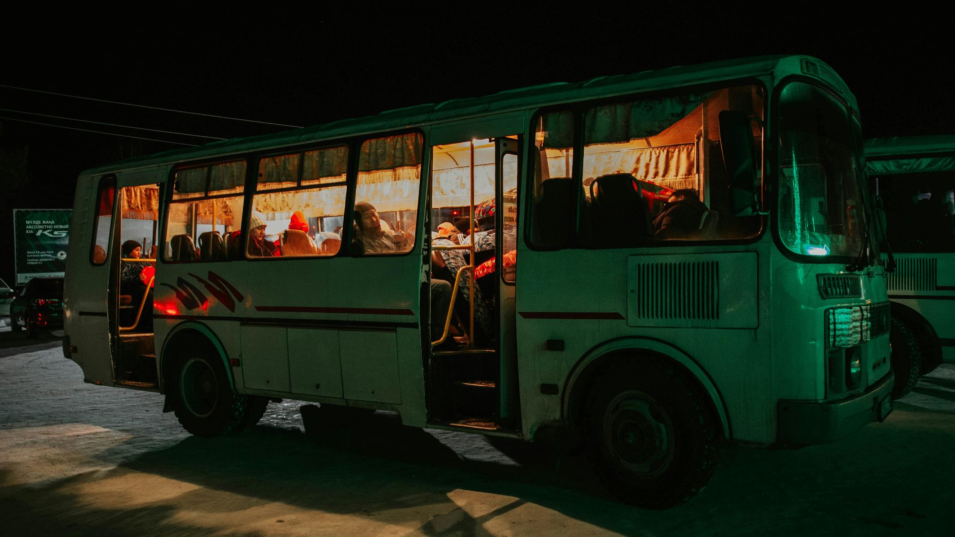 A bus parked at night with passengers visible inside, creating a warm, inviting glow.