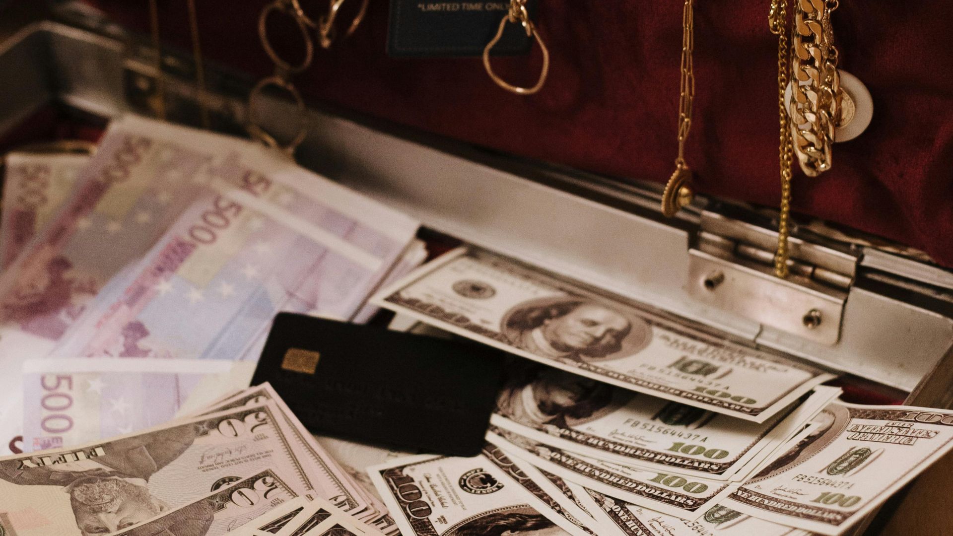 Open suitcase filled with cash, gold necklaces, and a sale tag, symbolizing wealth.