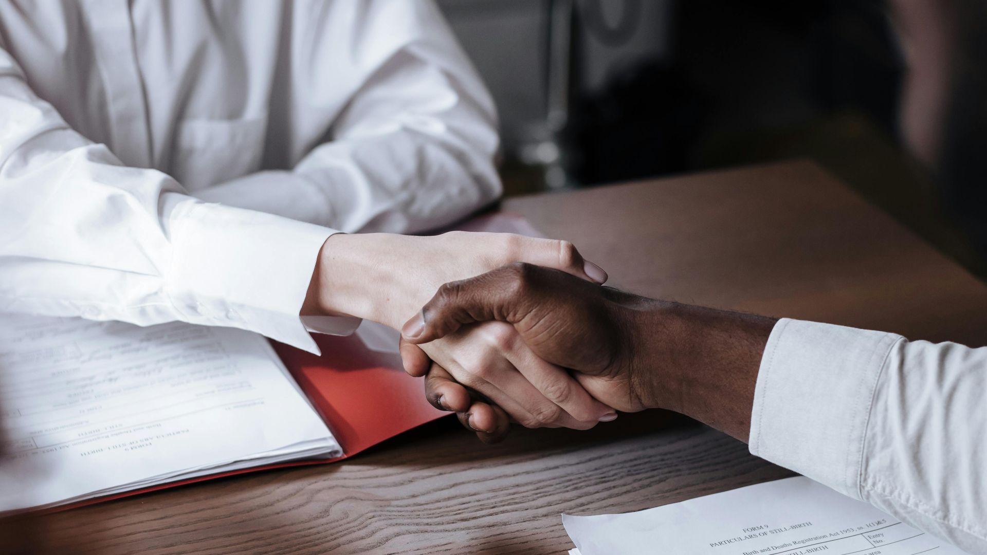 Close-up of a diverse business handshake over documents, symbolizing agreement and collaboration.
