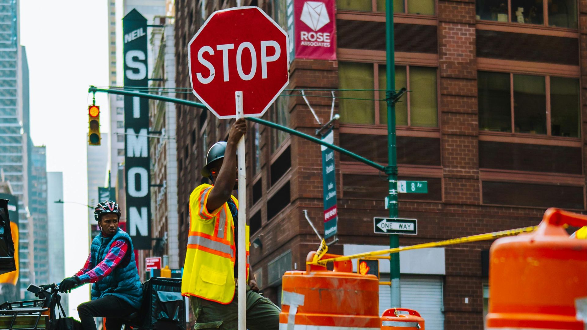 Man managing traffic in a busy urban construction zone with cyclists and skyscrapers.