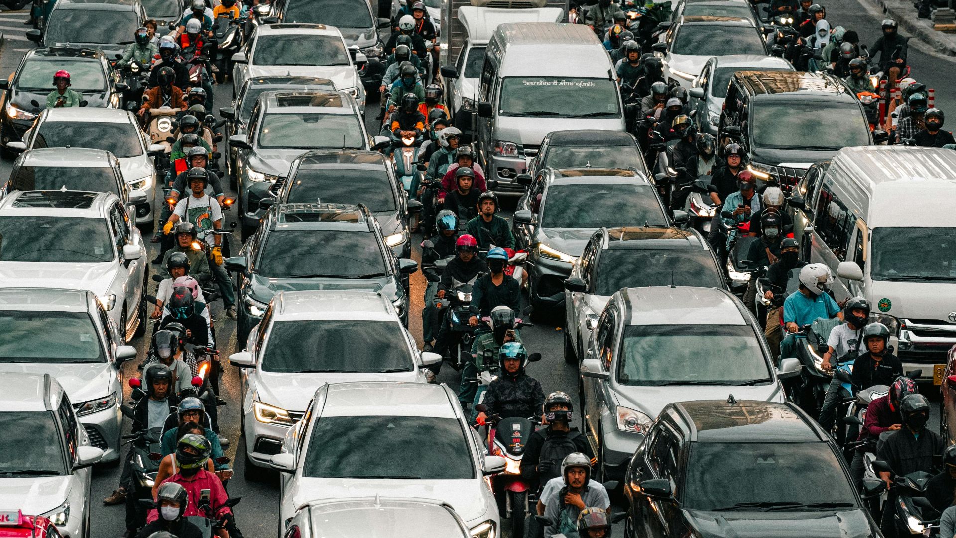 Aerial view of heavy traffic congestion, capturing cars, motorcycles, and people on a bustling city street during the day.