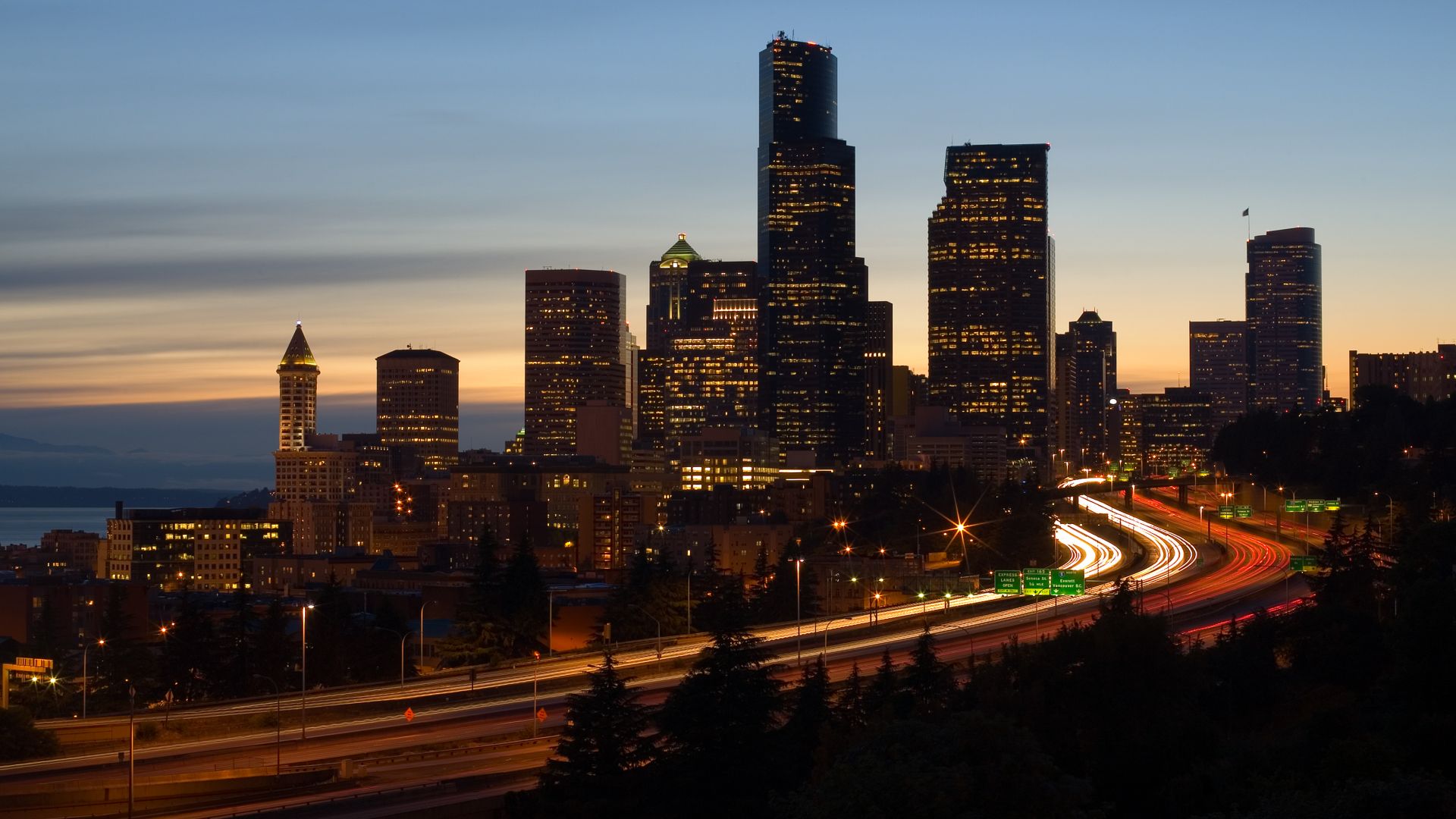 The skyline of Seattle, Washington at dusk.  Interstate 5 is the freeway that cuts through downtown and Puget Sound is visible to the left.
