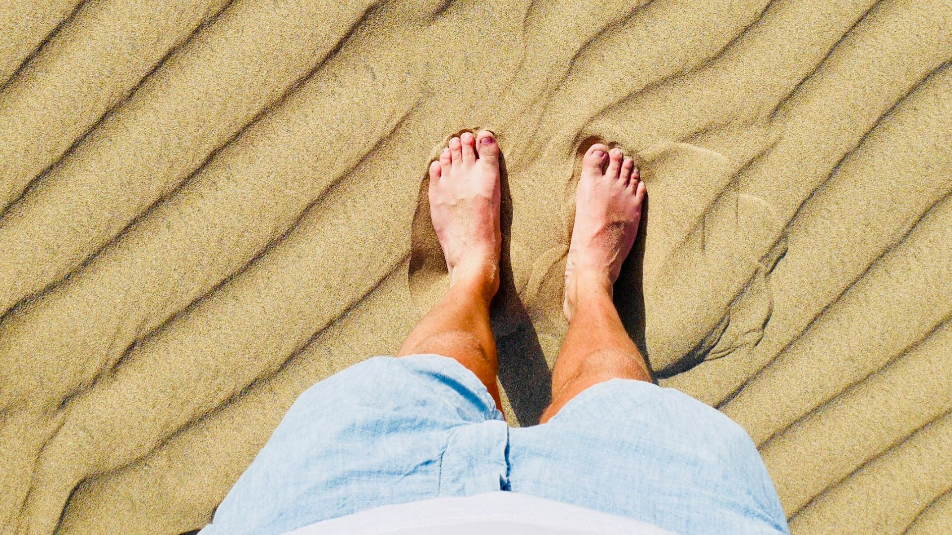 person in white pants standing on brown sand