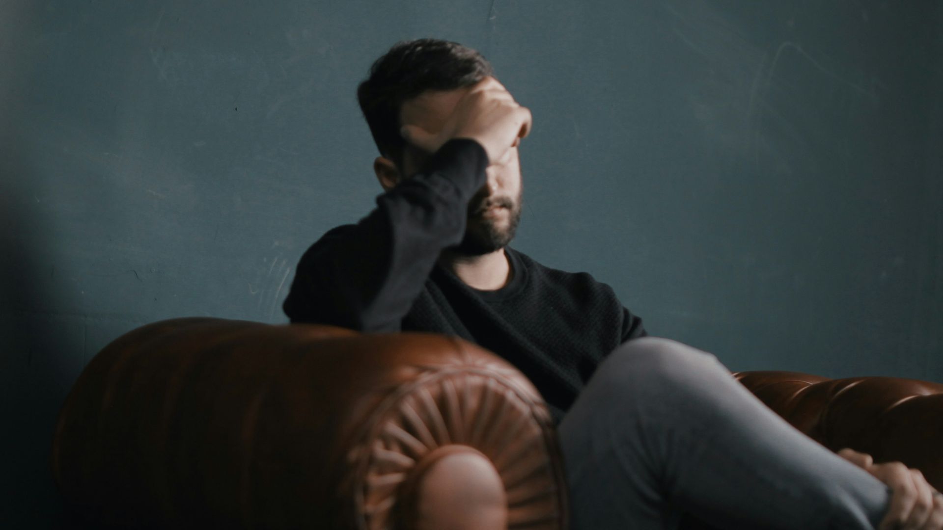 a man holds his head while sitting on a sofa