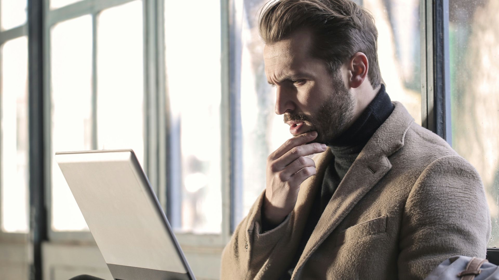 man holding his chin facing laptop computer