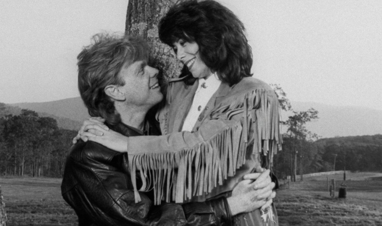 Getty Images - 50429333 - Former cast members of the TV show The Waltons Lisa Harrison & husband Jon Walmsley cuddling by tree during the opening of the Walton Mountain Museum.