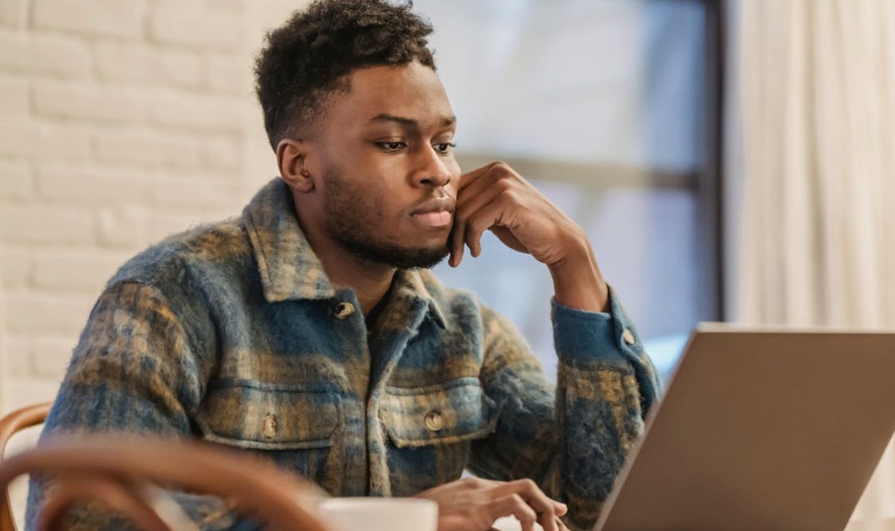 Serious black man working on laptop in workspace