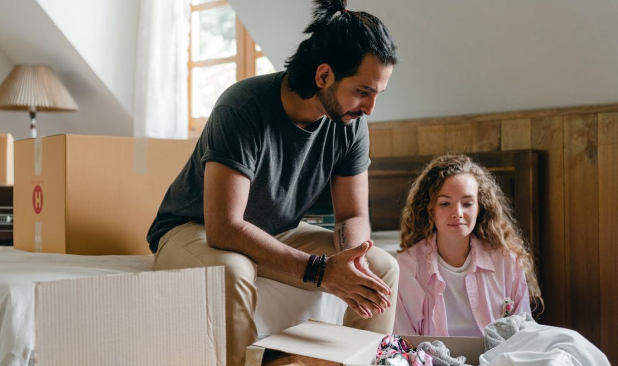 Diverse couple unpacking carton boxes during relocation at new home