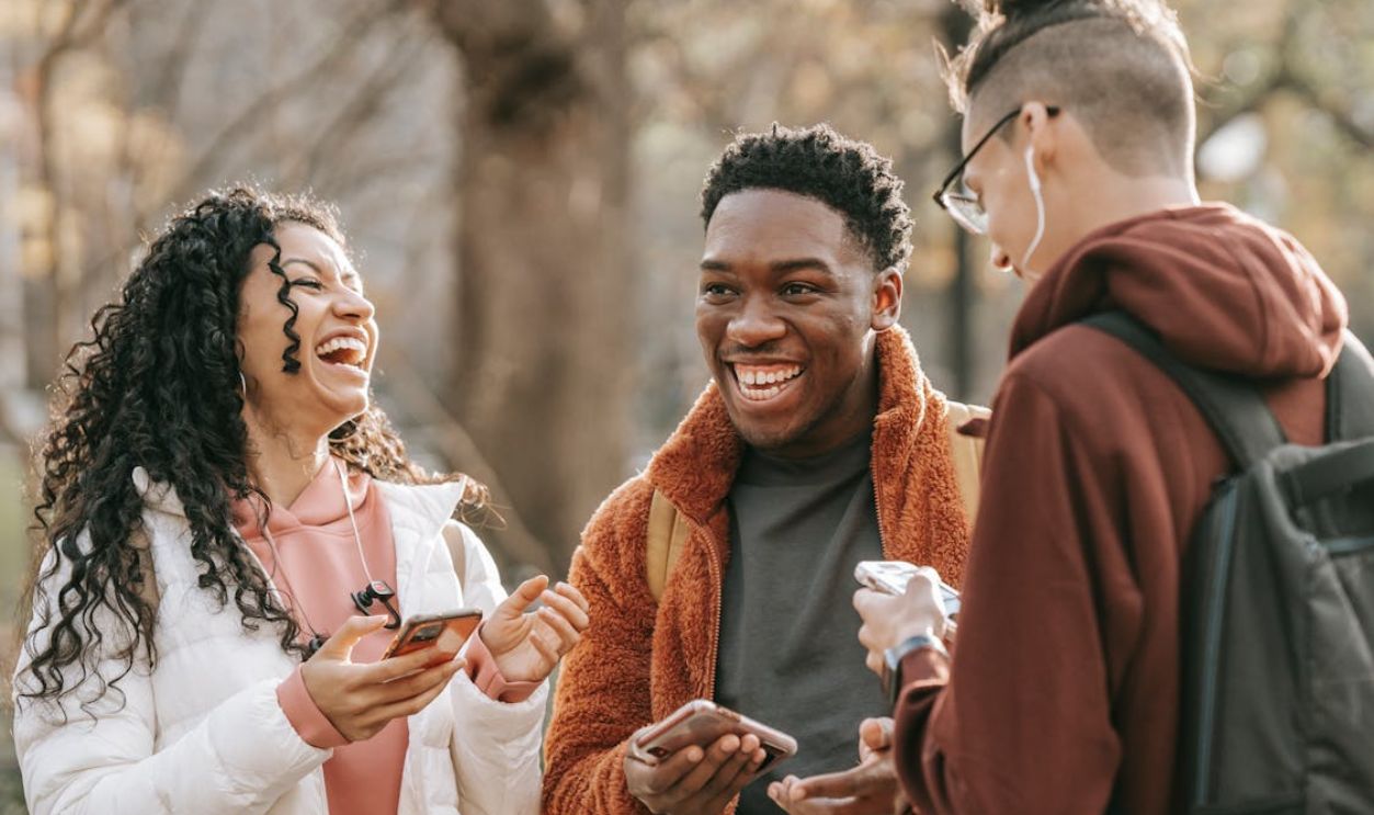 Laughing diverse friends with smartphones in park