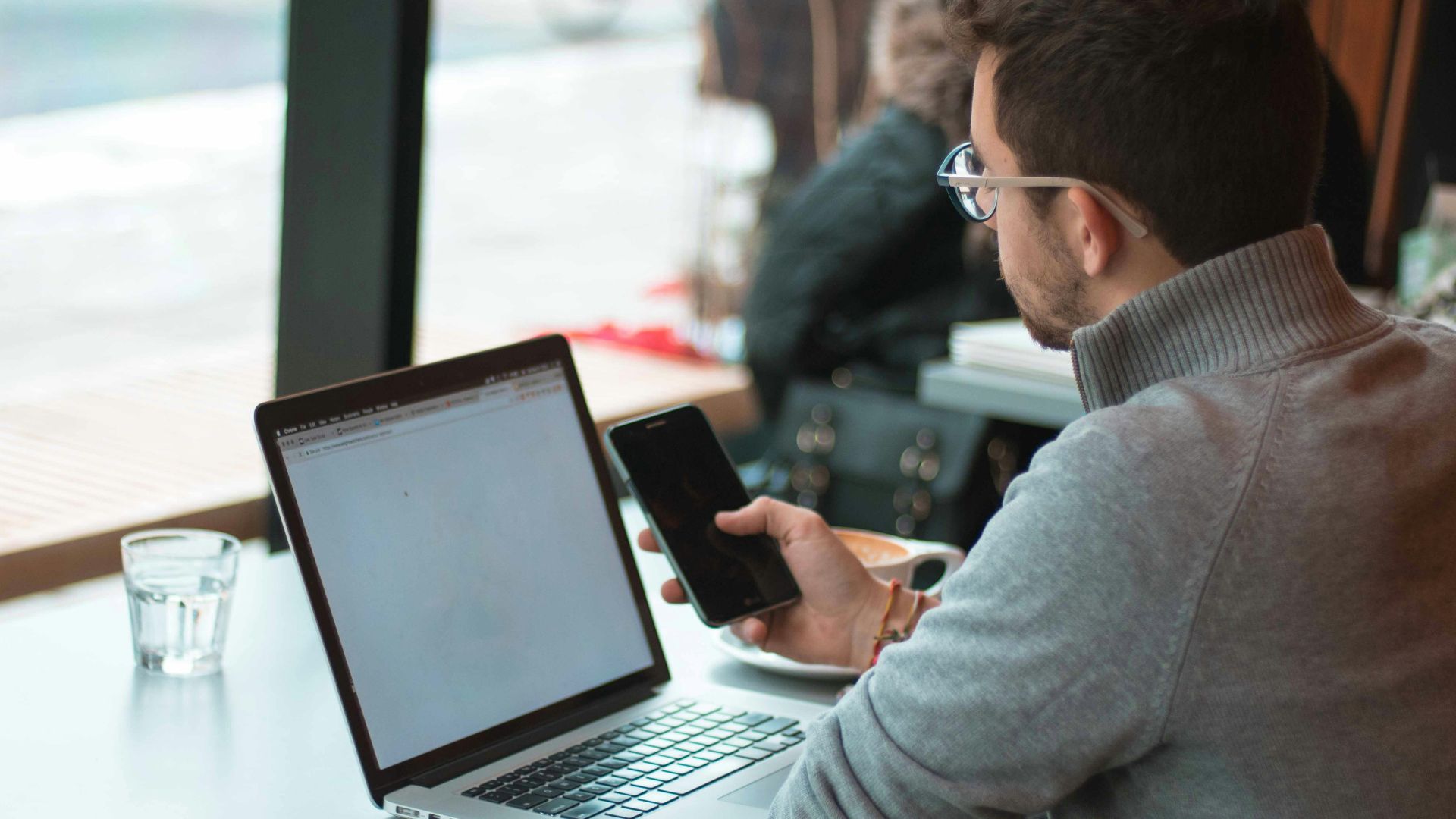 man sitting near table with laptop and smartphone near window