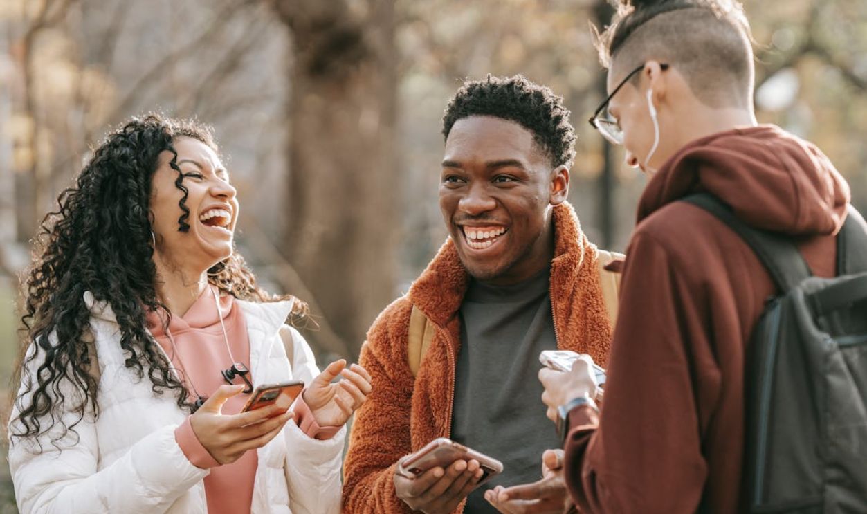 Laughing diverse friends with smartphones in park